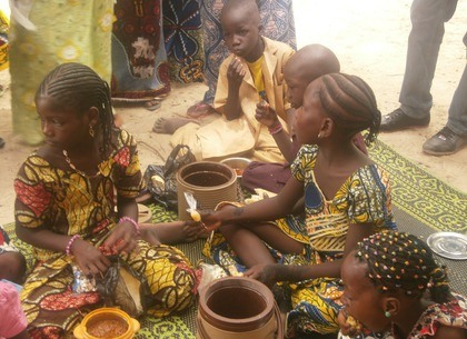 kinderen in kleurrijke kleding, meisjes met ingevlochten haar, zittend op een geweven mat eten uit aarde werken potten